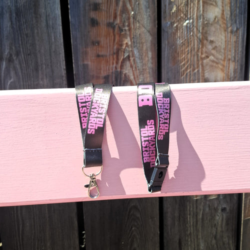 A dark green lanyard with the pink 'Bristol Dockyards' logo draped over a pink wooden surface.