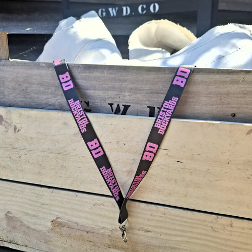 A dark green lanyard with the pink 'Bristol Dockyards' logo draped over a wooden surface.