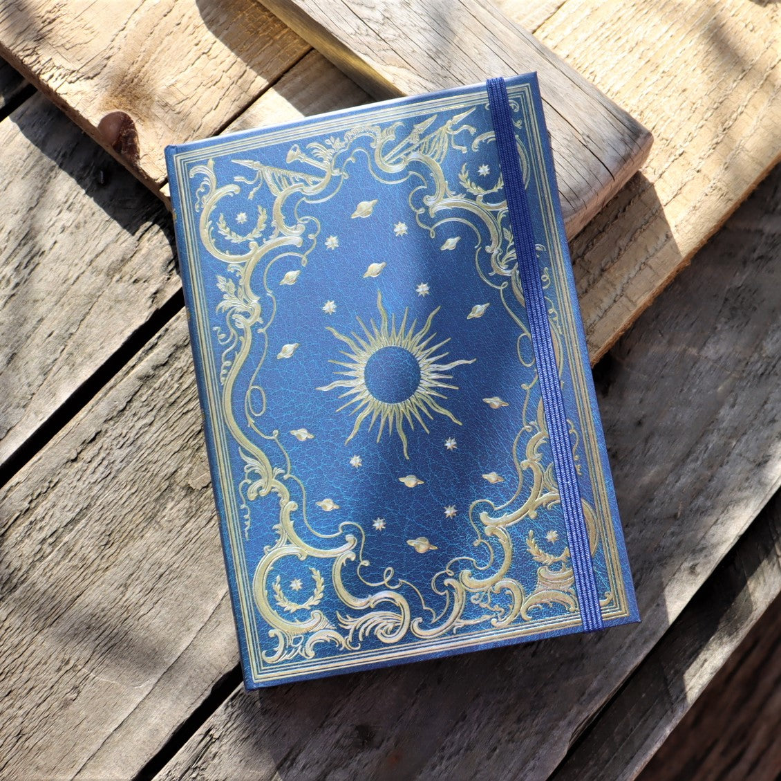 A dark blue and gold hardcover journal with a sun and stars pattern on the cover, placed on a wooden surface.