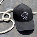 A black cap with the 'Go Aloft! Hold Fast' logo printed in white, placed on a surface with a coiled white rope beside it.