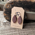 Wooden leaf shaped earrings on a card with JR logo on a rustic wooden background