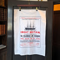 A white cotton tea towel with a print of a Victorian advertising poster for the SS Great Britain's voyages to Australia in 1873. The poster design includes a line drawing of the ship and text in red and black advertising prices and destinations.