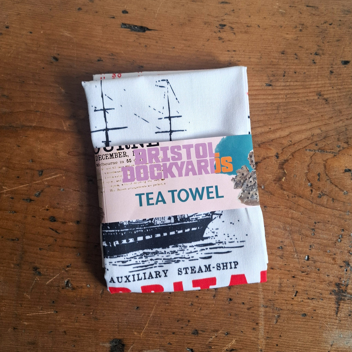 A folded Melbourne tea towel with a colourful band reading 'Bristol Dockyards: Tea Towel'