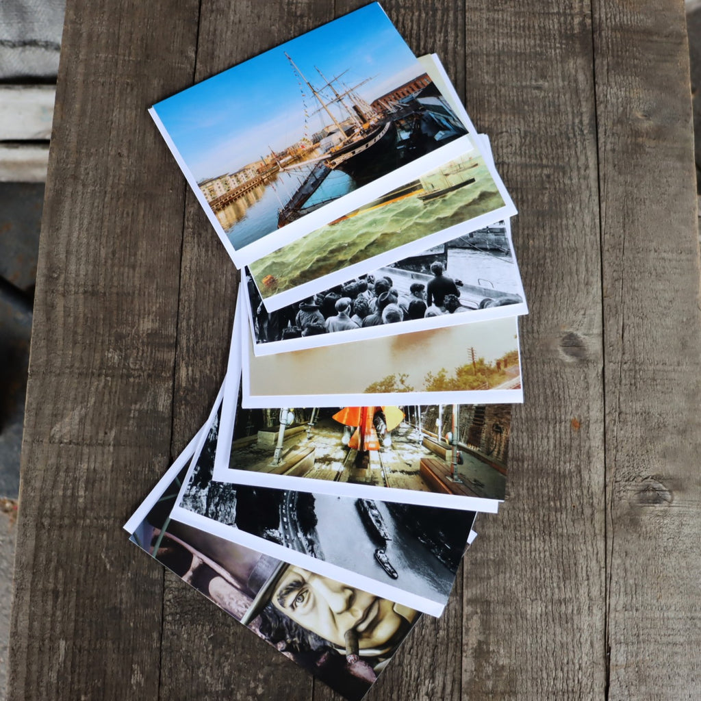 A stack of greetings cards with various images of a ship, both historical and modern, placed on a wooden surface.