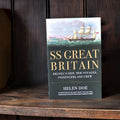Paperback book titled 'SS Great Britain' by Helen Doe, featuring an illustration of the SS Great Britain on the cover, placed on a wooden shelf.