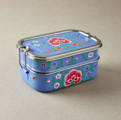 A metal and enamel tiffin style lunch box with a violet surface and colourful hand painted flower design. 