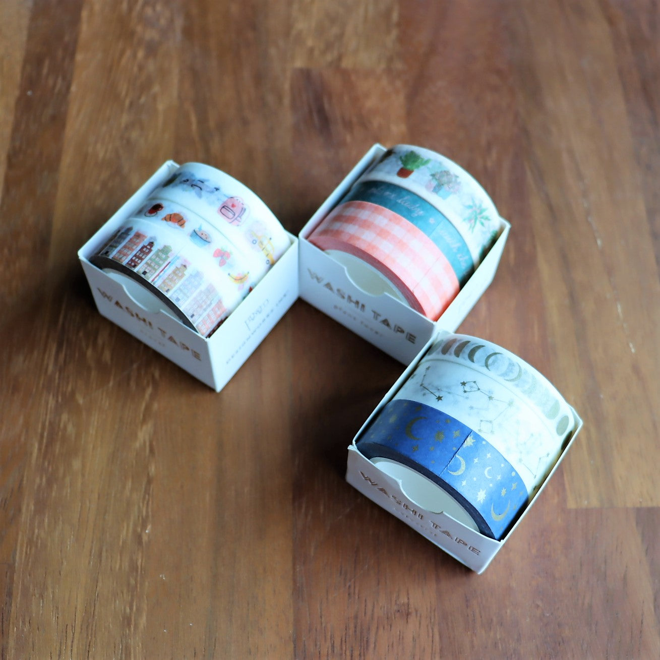 Nine rolls of washi tape with different designs, placed side by side on a wooden surface.