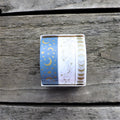 Three rolls of washi tape with different designs, placed side by side on a wooden surface.