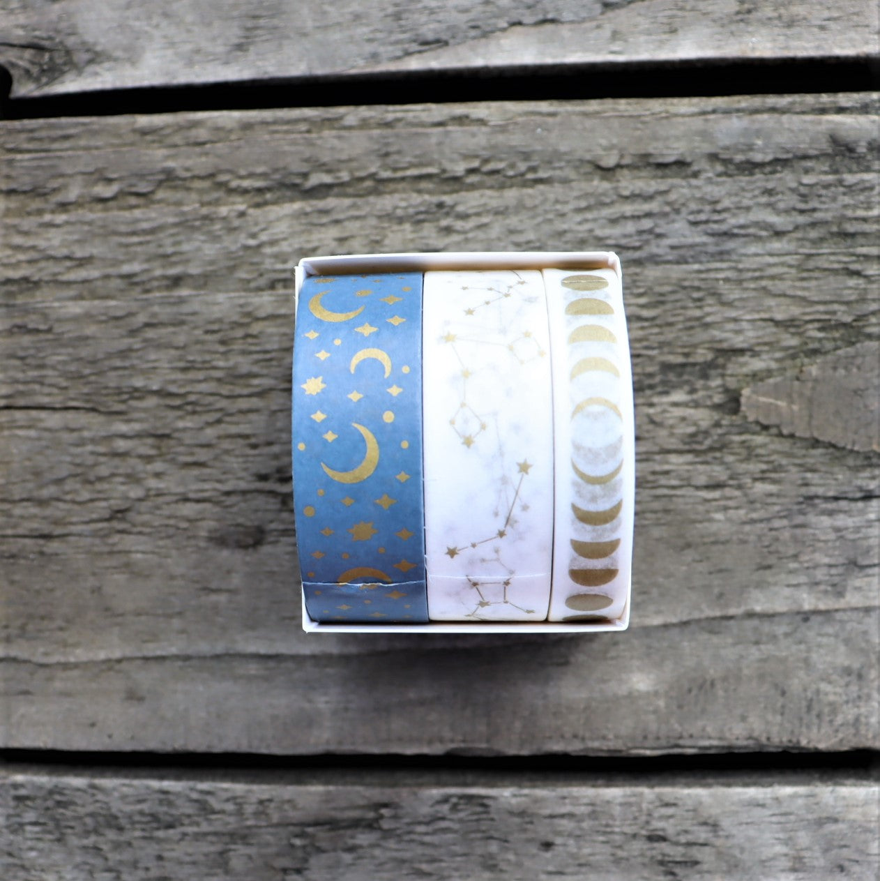 Three rolls of washi tape with different designs, placed side by side on a wooden surface.